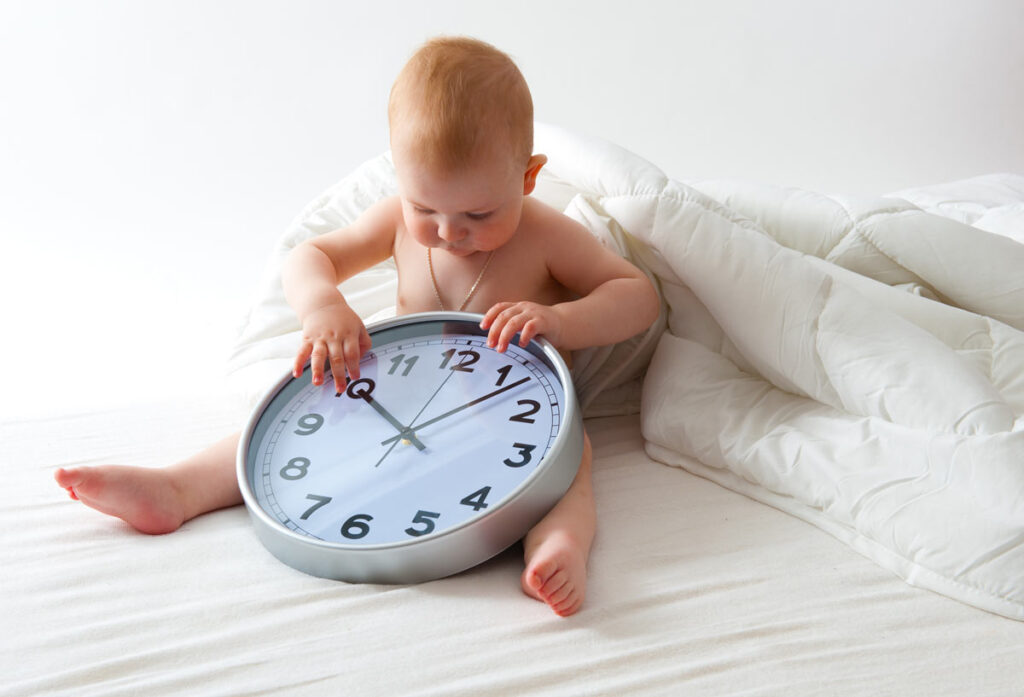 Baby sitting next to a clock